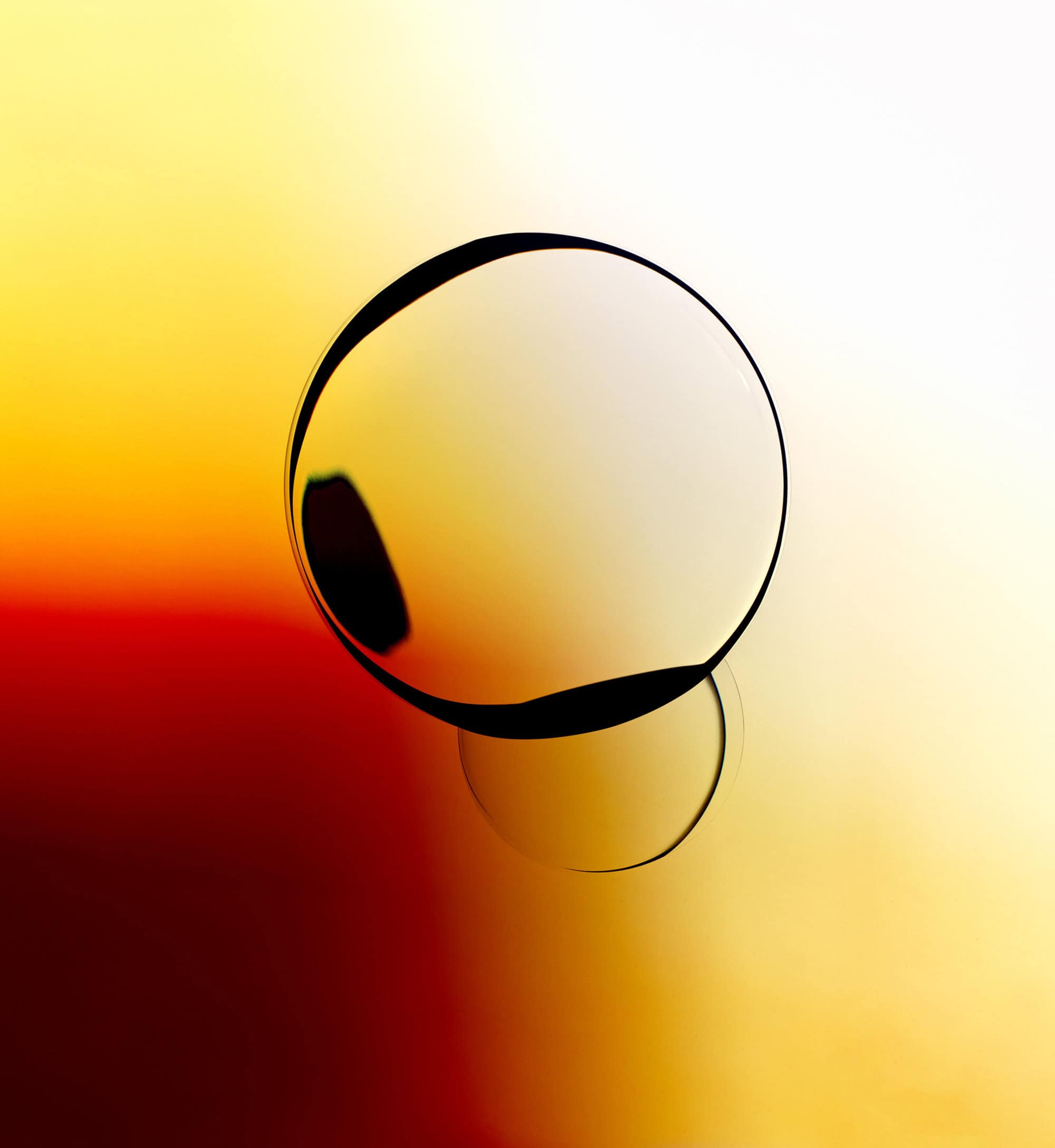 Abstract image of a transparent sphere reflecting red, orange, and yellow light. The sphere sits on a reflective surface.