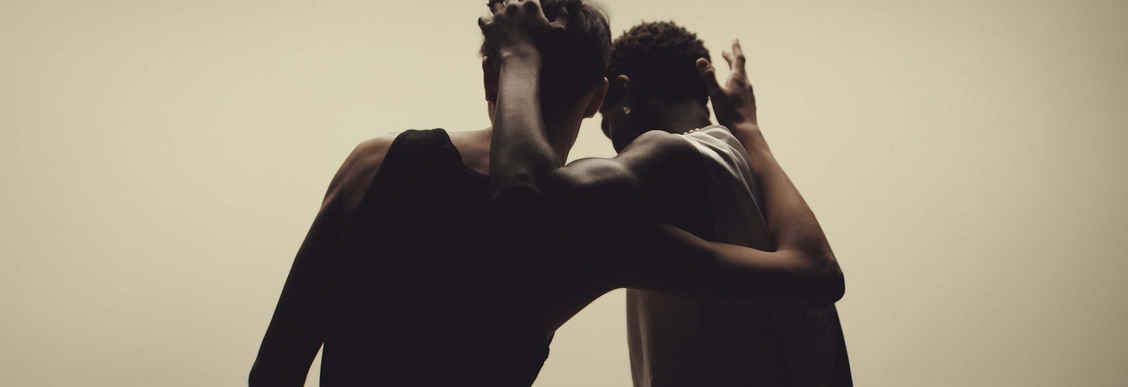 Two people embracing in a close-up shot with soft lighting, showcasing a moment of connection against a neutral background.