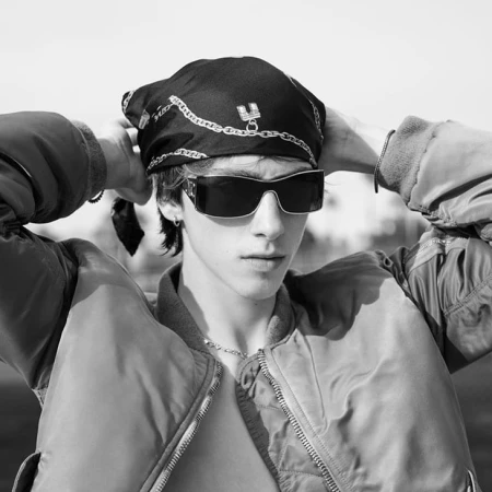 Close-up portrait of a male model wearing sunglasses, a printed bandana, and a bomber jacket for Celine.
