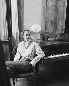 Model seated on a chair indoors next to a piano wearing a collared shirt and belt, for Tod's Pre-Fall 2024 campaign.