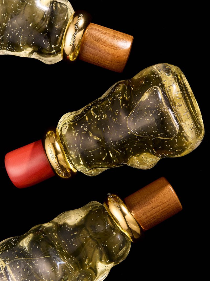Three perfume bottles with clear glass and wooden tops are positioned against a black background in a beauty product shot.