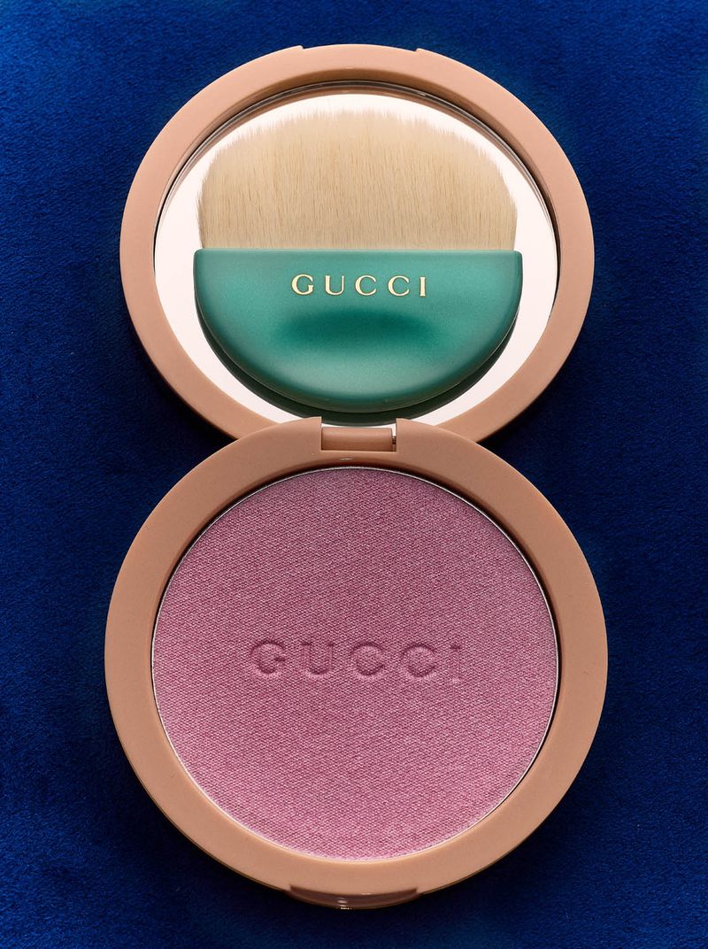 Gucci blush compact with mirror and brush, showcasing luxury beauty product on a textured blue background, close-up.