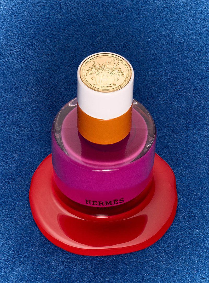 Artistic studio shot of a perfume bottle with a layered, colorful design, featuring shades of white, orange, pink, and red.