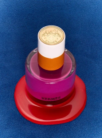 Artistic studio shot of a perfume bottle with a layered, colorful design, featuring shades of white, orange, pink, and red.