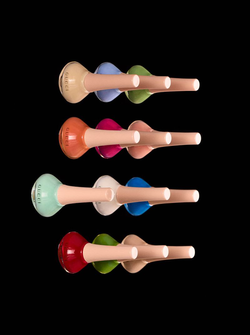 Arrangement of colorful Gucci nail polish bottles with wooden holders in a studio shot, presented against a stark black backdrop.