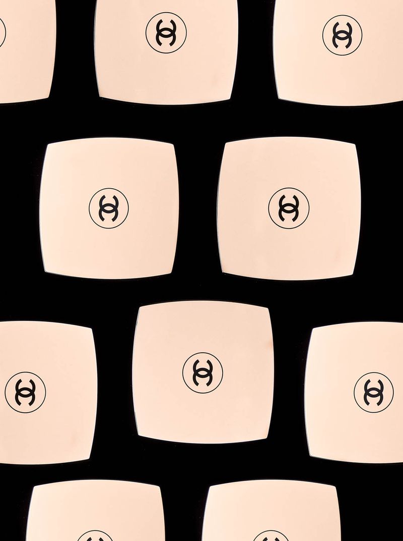 Multiple Chanel powder compacts arranged in a grid pattern against a black background. Cosmetic product photography, clean, beauty.