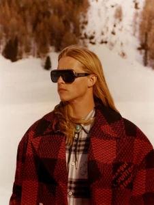 Model with long blonde hair wearing sunglasses and a red patterned coat in a snowy landscape for Louis Vuitton
