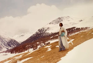 Model wearing a white fringe coat and blue handbag standing on a snow-covered mountain slope for Louis Vuitton