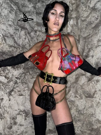 Woman wearing handbag fashion with black opera gloves, belt and thigh-highs, posing in front of textured grey stone-like wall.
