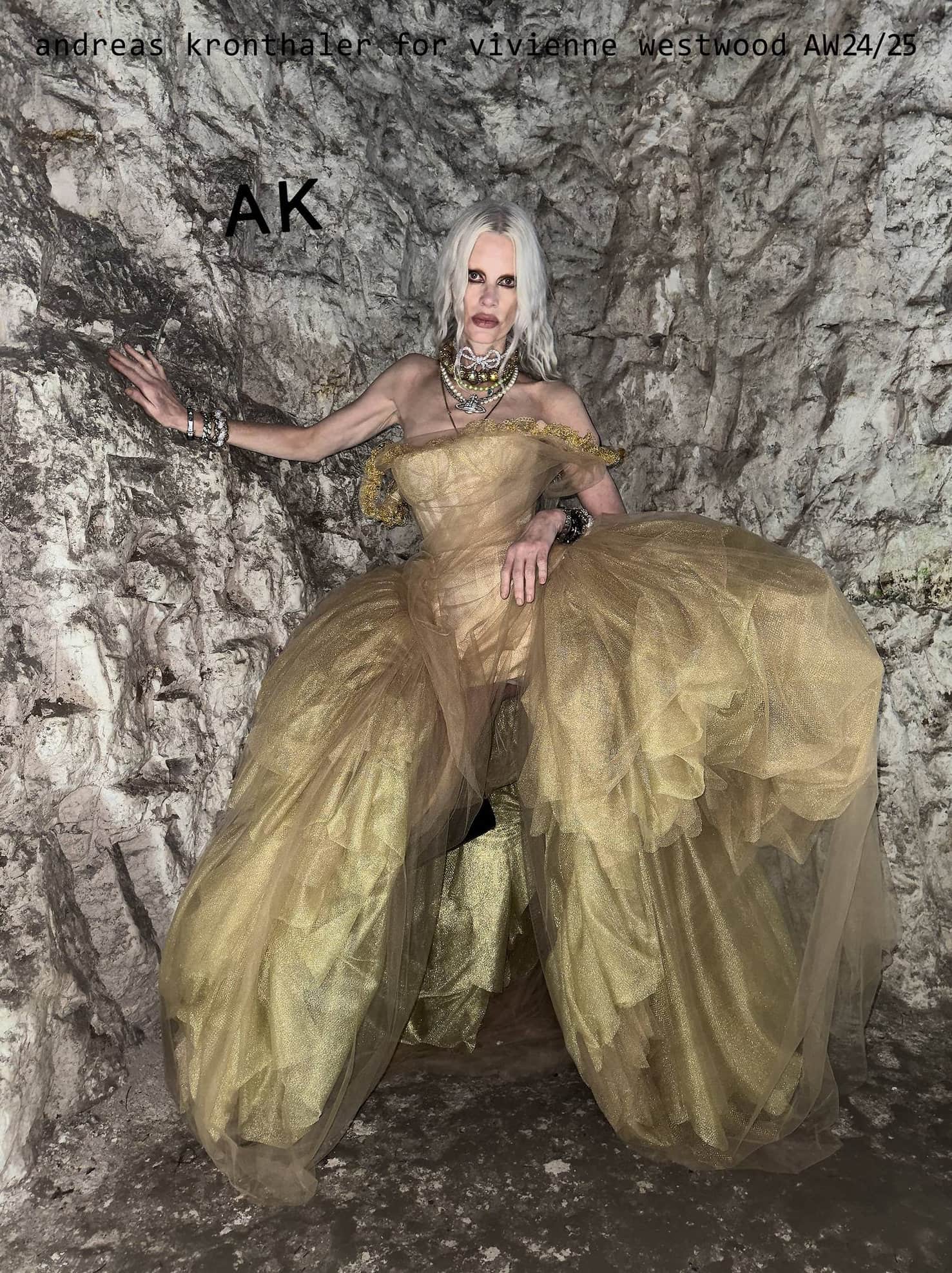 Fashion image featuring a pale-skinned woman in a gold tulle gown posing inside a stone structure, showcasing high fashion in a unique setting.