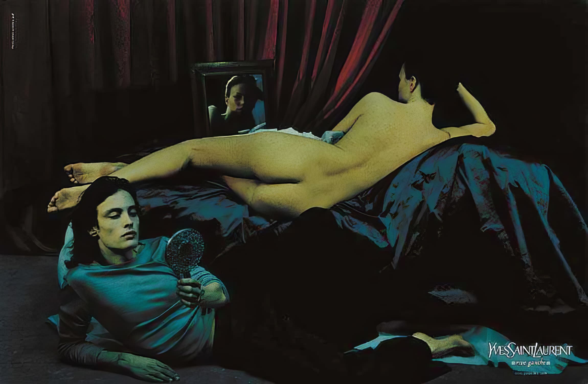 Fashion photography features an adult man and woman on a dark bed with a mirror. YSL logo is visible, styled with red curtains.