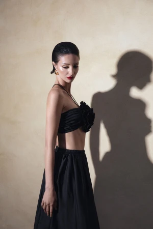 Model in black two piece outfit with slicked back hair posing against textured wall with prominent shadow
