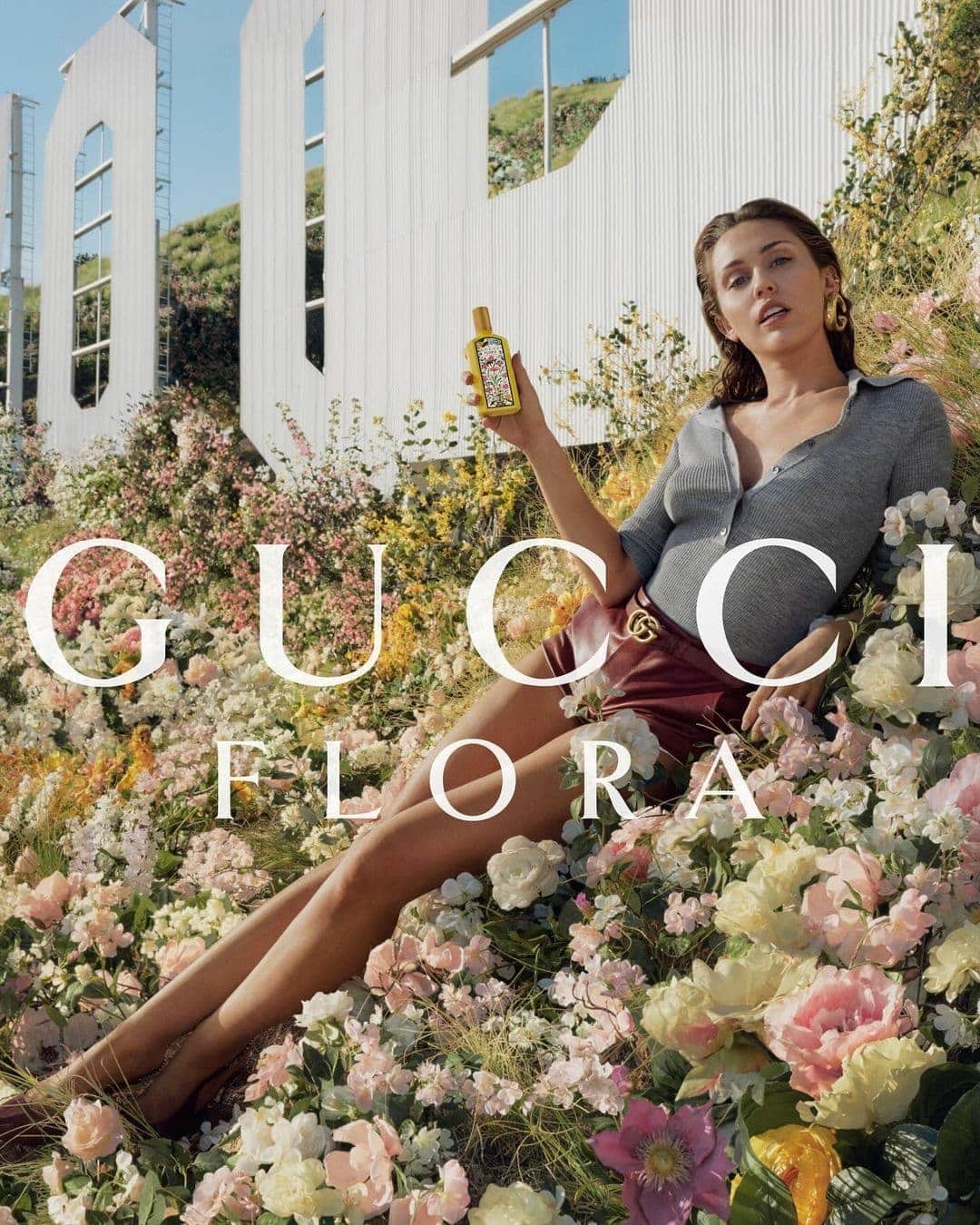 Adult female model posing with Gucci Flora perfume among flowers with the Hollywood sign in the background. Fashion advertising shot.
