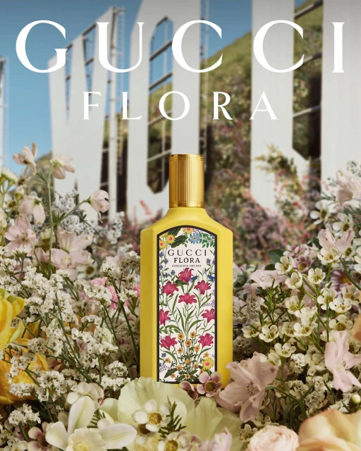 Gucci Flora perfume bottle sits among lush pastel flowers against a background of the Hollywood sign. Beauty and fragrance concept.