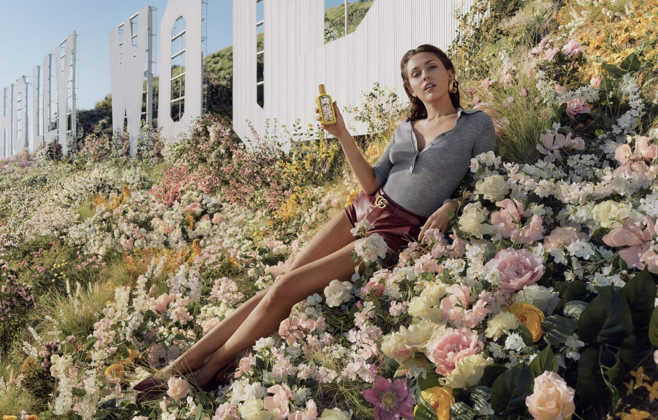 Woman poses with perfume in a field of flowers with the Hollywood sign in the background, creating a vibrant fashion editorial image.