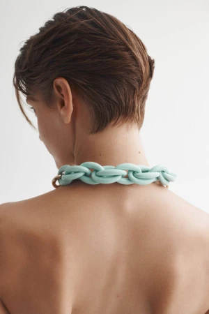 Adult female with short brown hair wearing a thick braided blue necklace against a stark white background in a medium studio shot.