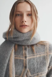 Portrait of a female model wearing a grey patterned cardigan and matching wool scarf against a plain studio background.