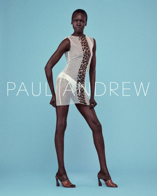 Fashion shot of an African female model wearing a sheer dress with leopard print detail, posing against a light blue background.