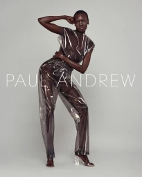 Model Alek Wek posing in transparent vinyl top and matching trousers against a neutral grey studio background