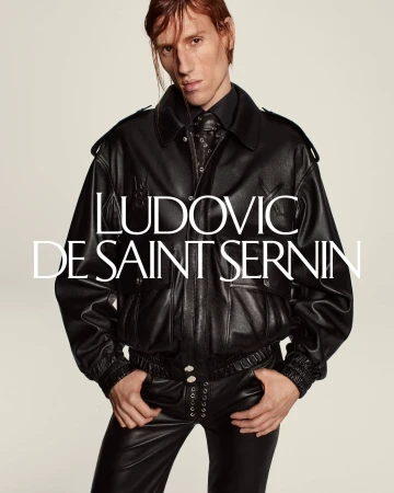 Fashion shot of a slender male model wearing a black leather jacket and pants, standing against a clean background with brand logo.