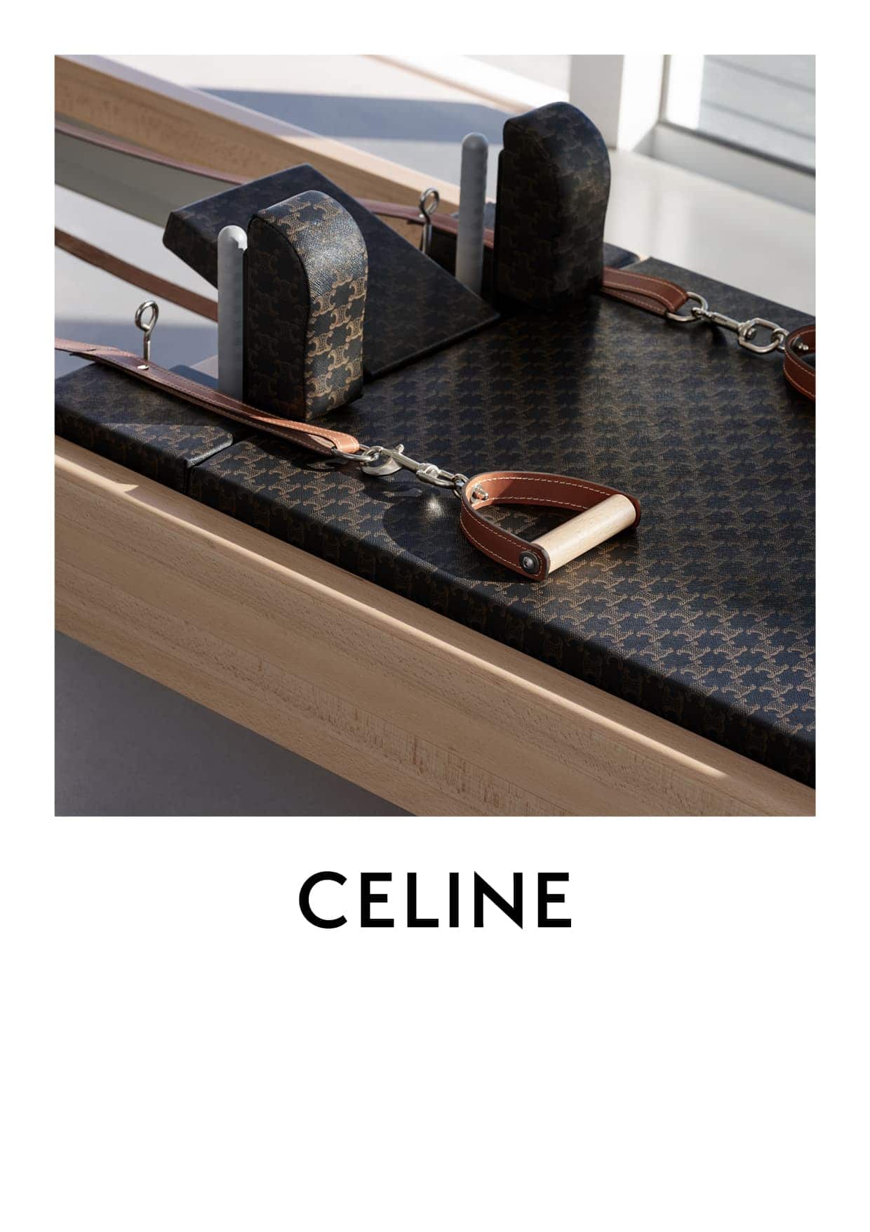 Close-up studio shot of Pilates reformer equipment with a patterned black and brown cover. Wood frame and metal accents are visible.