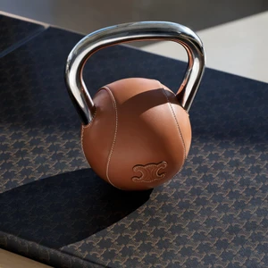 Tan leather kettlebell with a shiny silver handle resting on a patterned dark surface.
