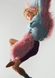 Model Hanne Gaby Odiele jumping in a blue sweater adorned with pink faux fur trim against a white background