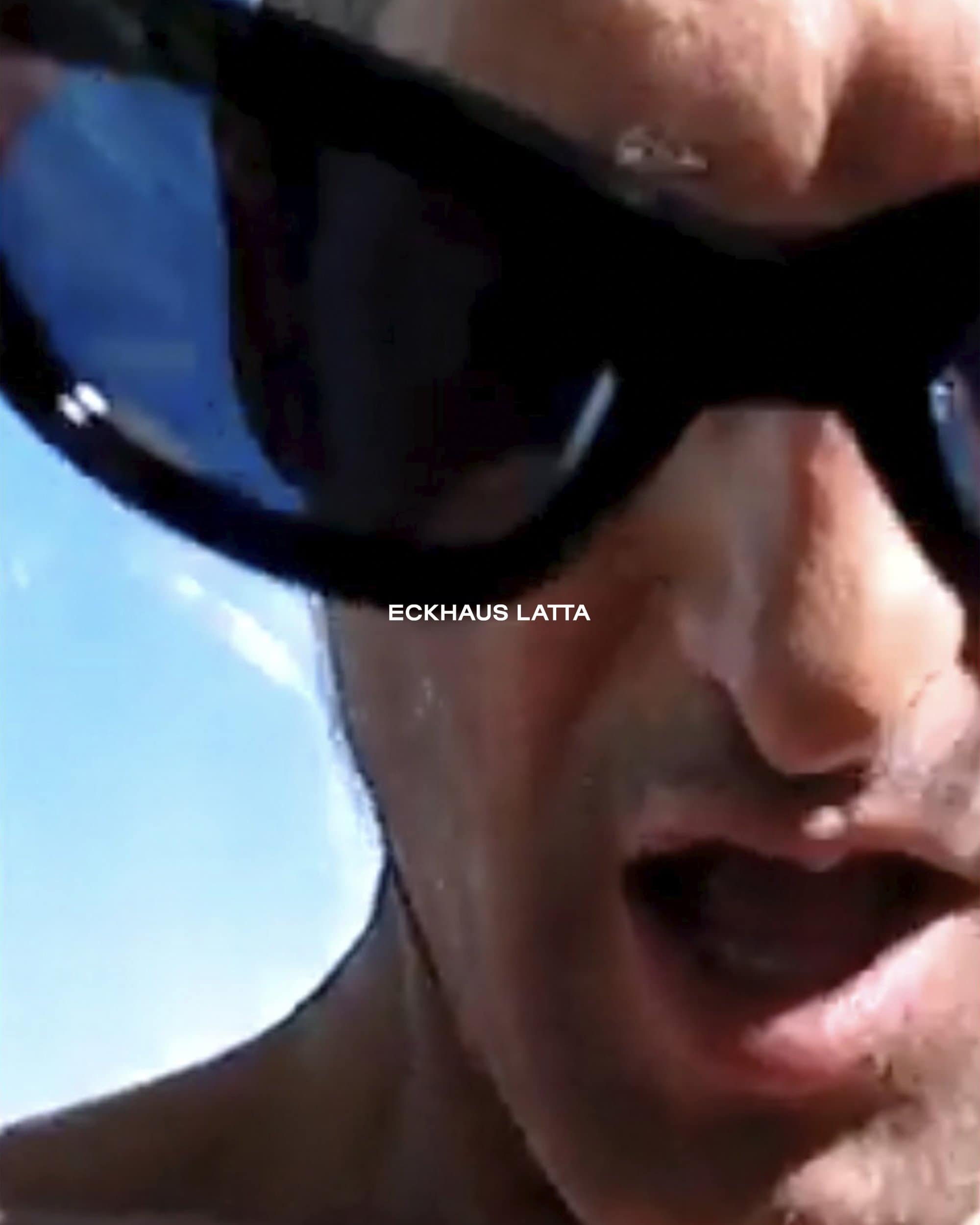 Close-up portrait of Tony Ward wearing black sunglasses against a clear blue sky for Eckhaus Latta Pre-Fall 2024.