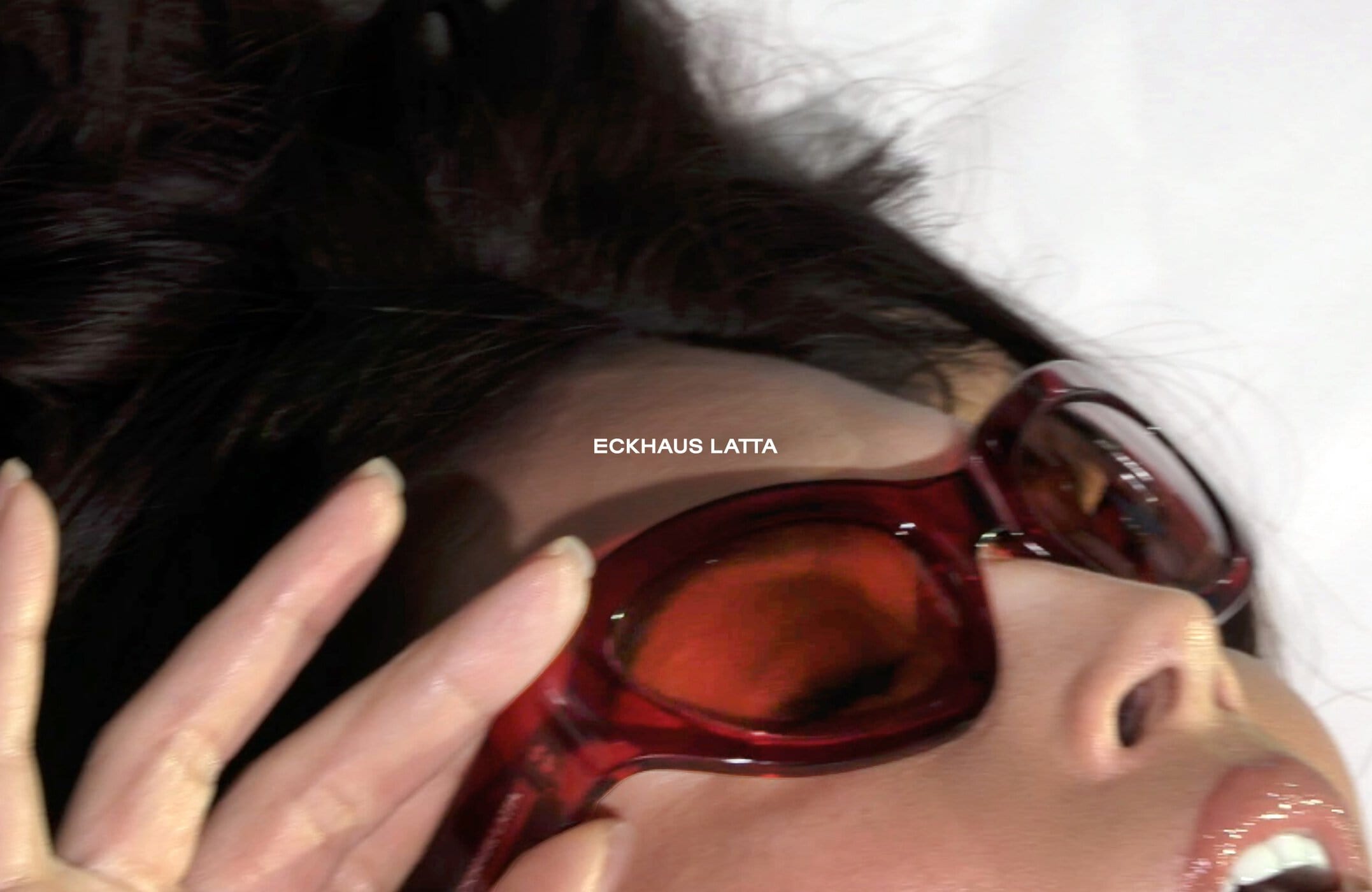 Brunette woman wearing red-framed sunglasses in an extreme close-up, face partially visible with a light complexion and glossy lips.