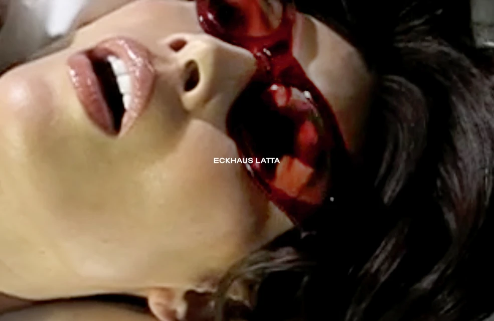 Close-up on a woman's face with glossy lips and dark hair, featuring stylized red makeup around the eyes in a beauty context.
