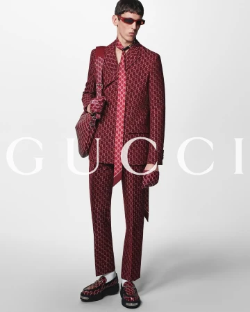 Model in printed burgundy suit holding matching shoulder bag and wearing sunglasses against a light background