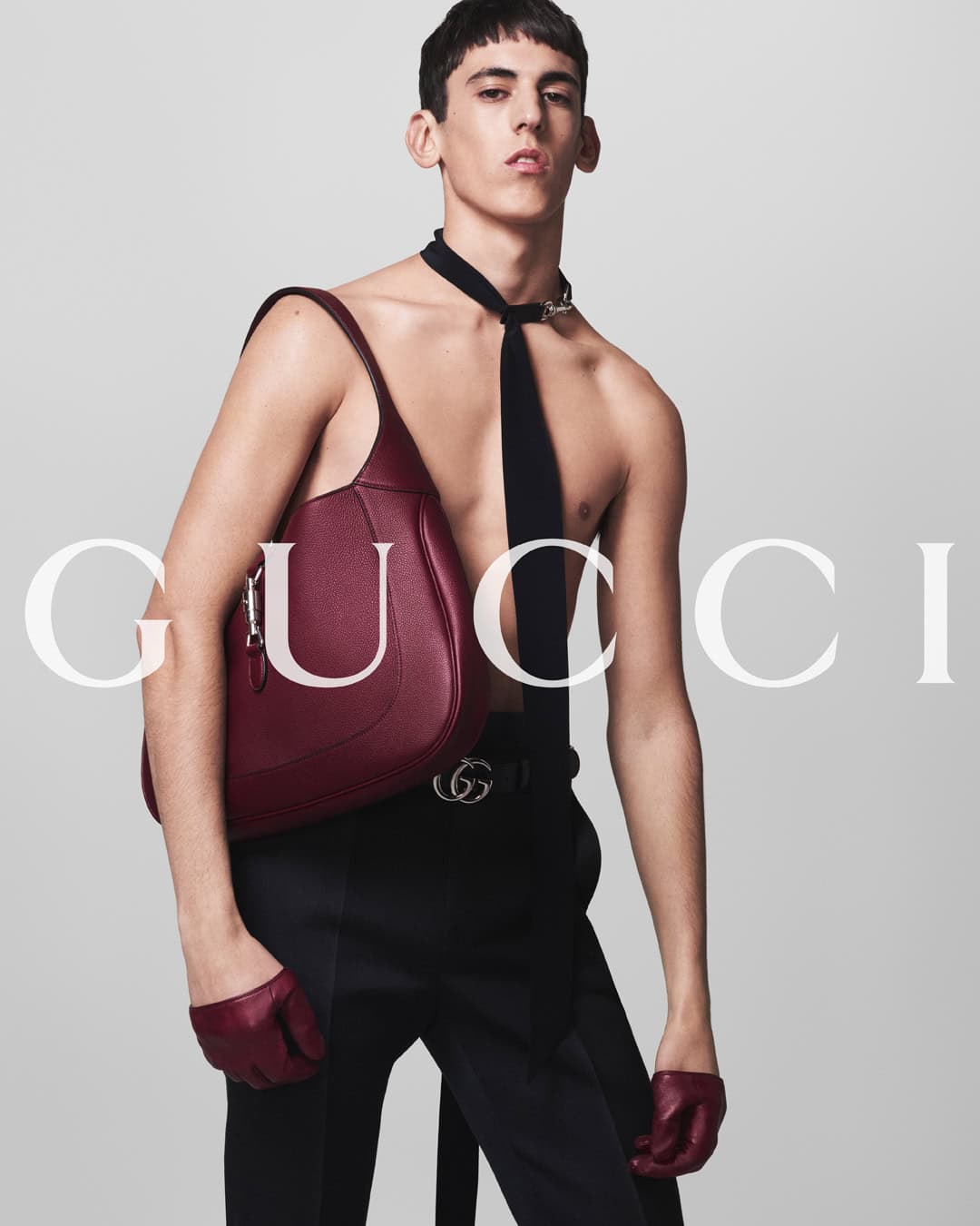 A fashion shot showcases a slender man with a Gucci handbag over his shoulder, posing with a stern expression against a neutral background.