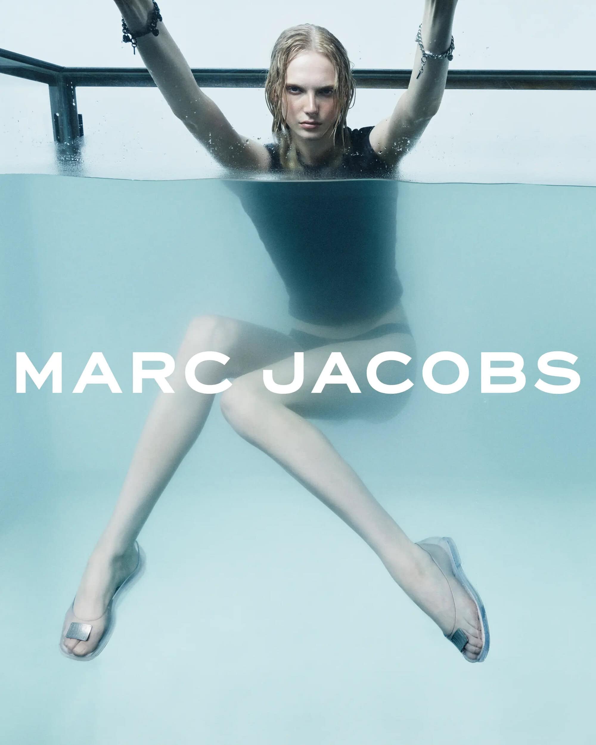 Fashion advertisement of a woman underwater wearing a black top and clear heels with the brand name MARC JACOBS in large white letters.