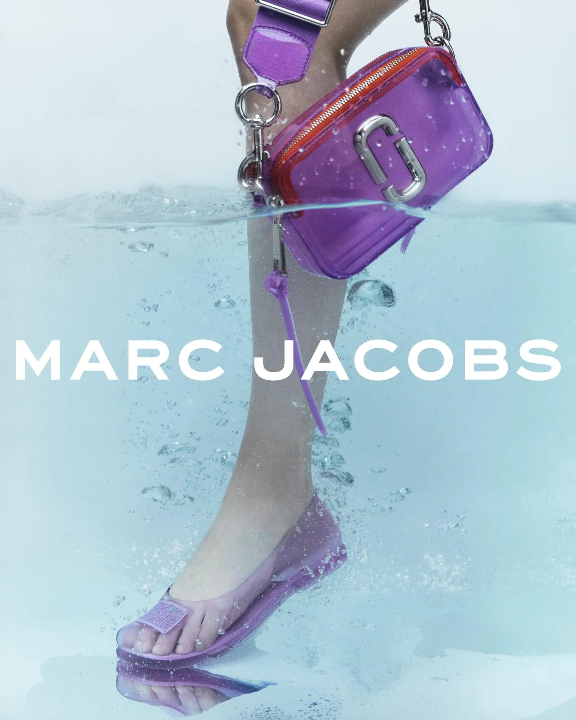 Fashion product shot featuring a Marc Jacobs clear purple purse with silver hardware, a matching shoe, and a person's leg submerged in water.