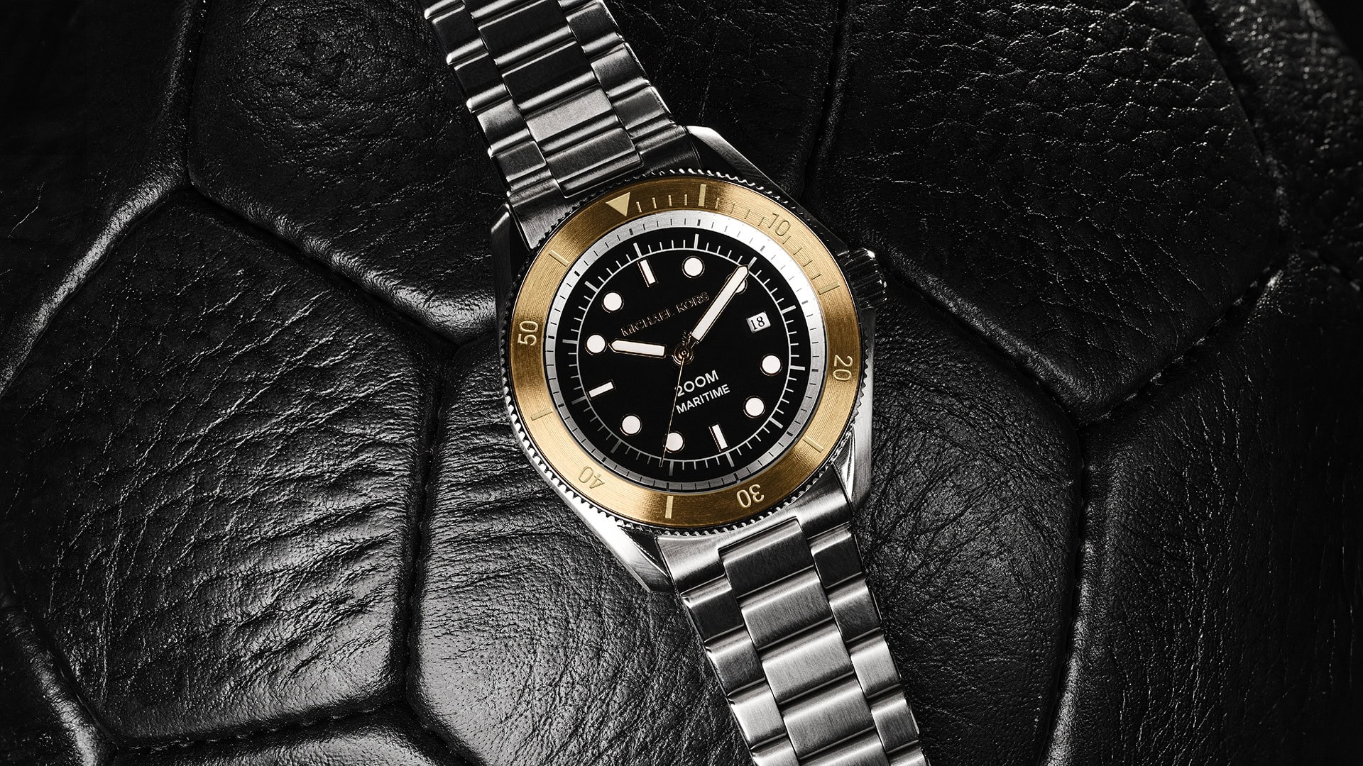 Wristwatch on a textured surface shows a stainless steel band, gold bezel, black dial, and date window for a luxury aesthetic.