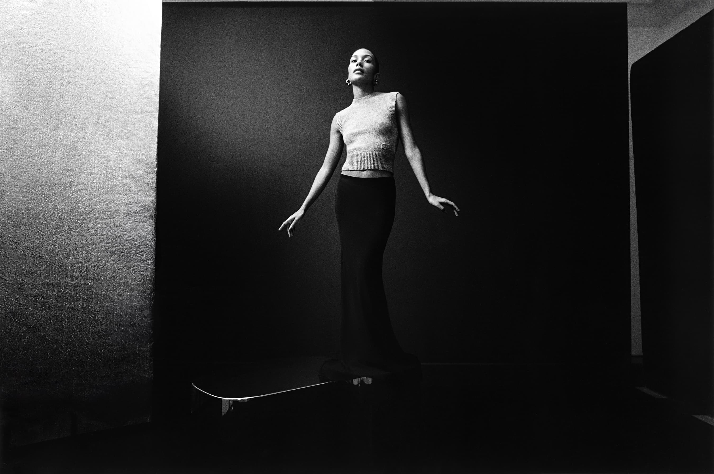 Elegant black and white portrait of a woman posing in a knit top and skirt with dramatic lighting and a minimalist background in a photo studio.