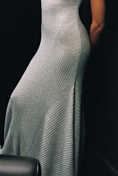 Close-up portrait of a model wearing a fitted grey ribbed knit dress against a dark background