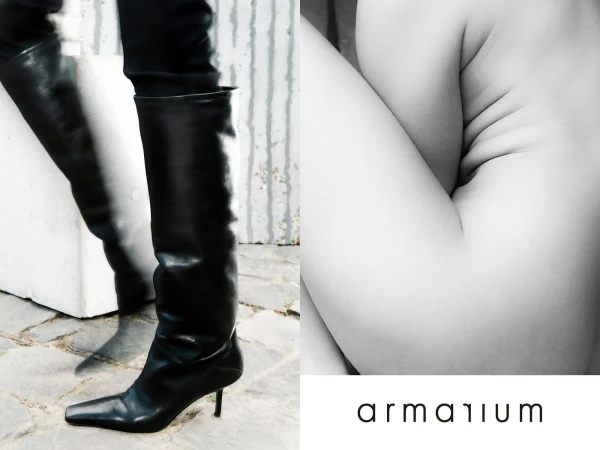 Black leather thigh-high heeled boots, legs, and abstract body art juxtaposed against a textured wall with designer brand logo.
