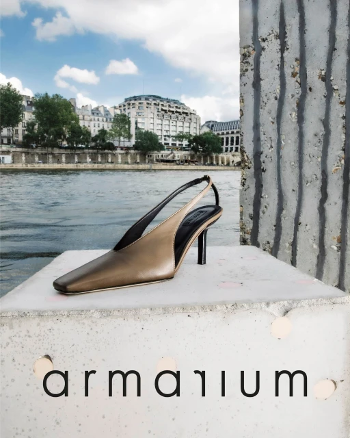 Fashion shot of a single slingback heel on a concrete block, featuring a river and urban buildings in the background under a cloudy sky.