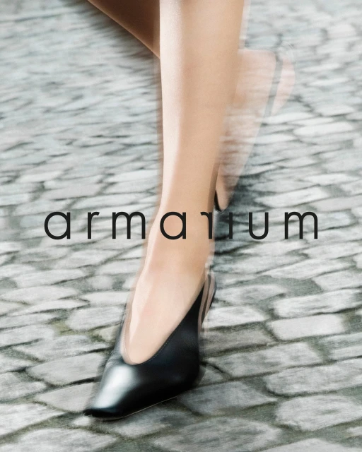 Fashionable black heeled shoes on a woman walking outdoors on a cobblestone path, showcasing a blurred motion effect. Brand: armarium.