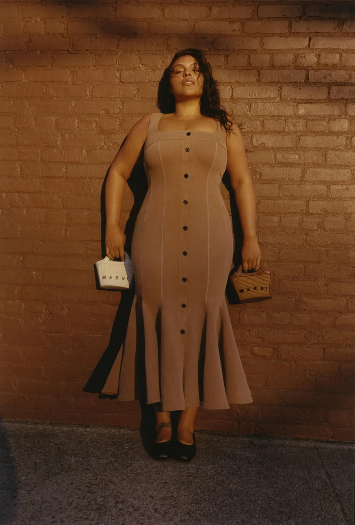 Model Paloma Elsesser wearing a brown buttoned dress standing against a brick wall for Marni