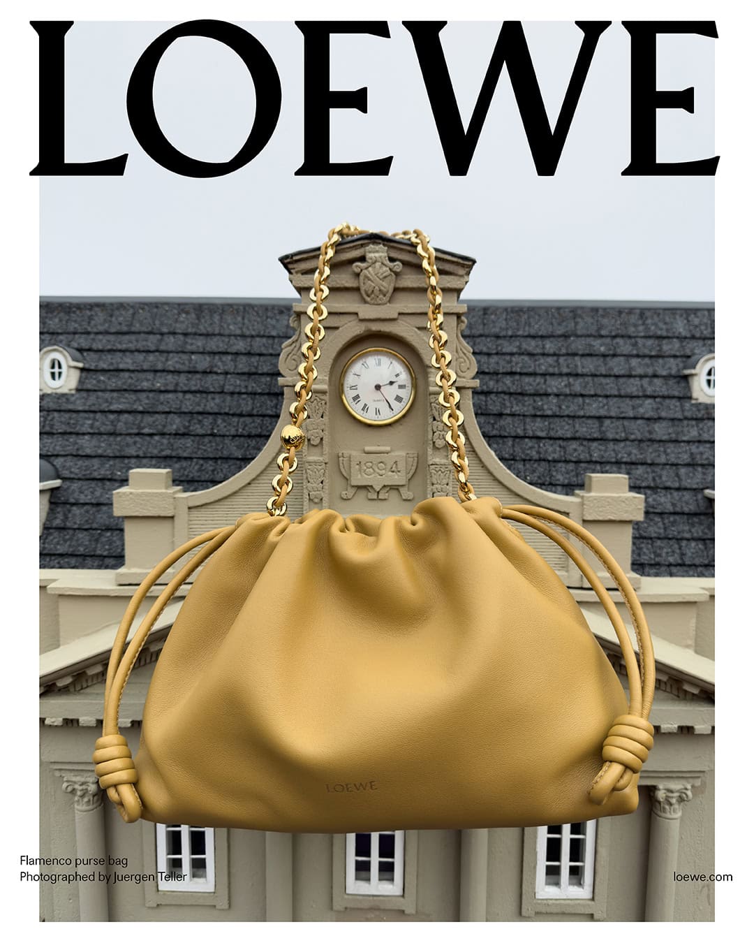 Loewe Flamenco purse bag with a golden chain strap, displayed in front of a miniature building with a clock and grey roof.