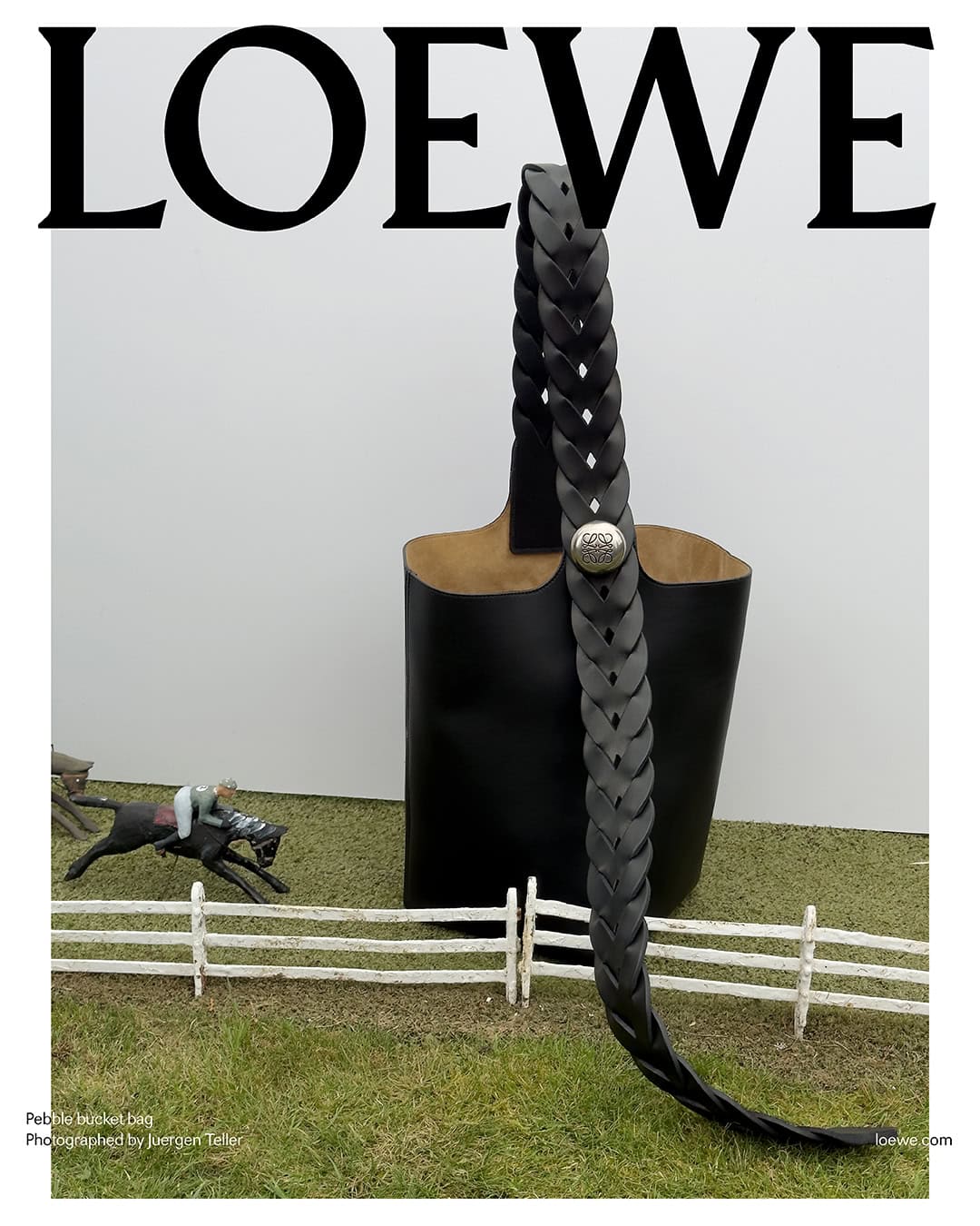 Loewe handbag with braided strap, studio shot with horse and rider miniature model on artificial grass, white background, minimalist.