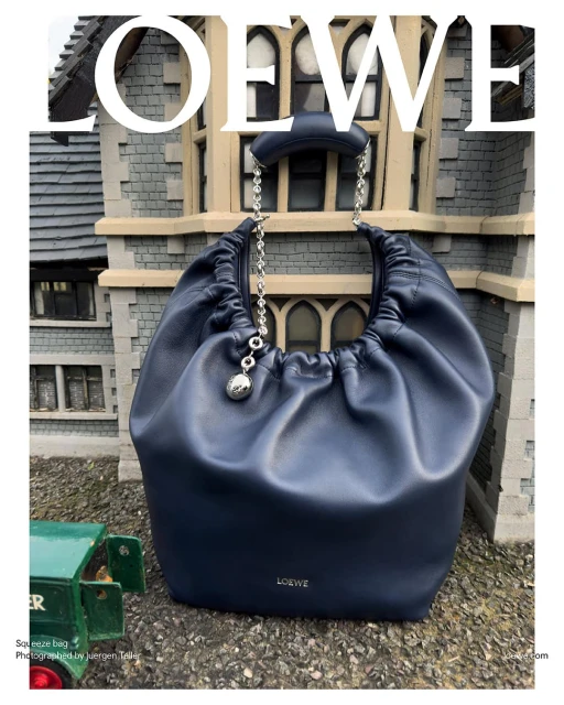 Navy blue Loewe Squeeze bag on display outdoors with a miniature building facade and green toy truck. Fashionable leather handbag.