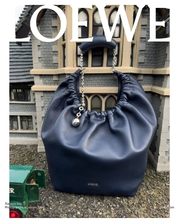 Navy blue Loewe Squeeze bag on display outdoors with a miniature building facade and green toy truck. Fashionable leather handbag.