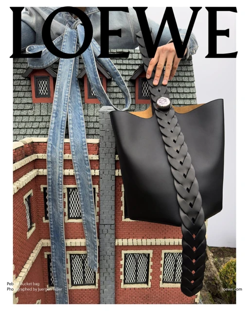 Loewe black leather bucket bag displayed against a miniature building, featuring a person in a denim jacket and oversized logo.