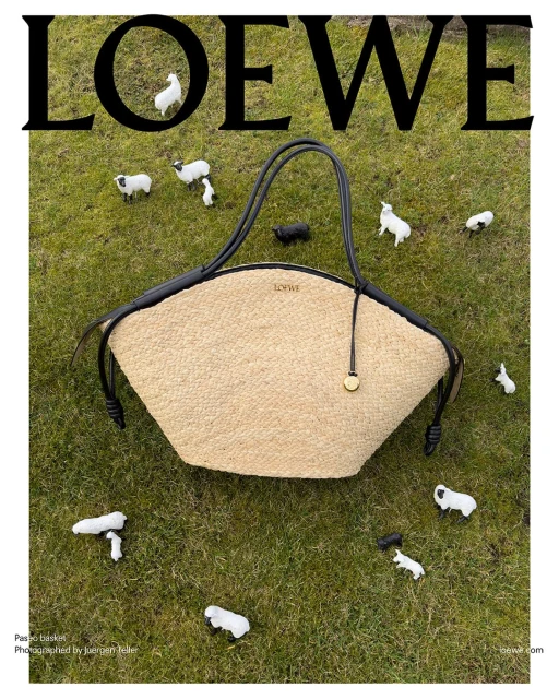 Loewe basket bag in a field of grass surrounded by small toy sheep, top-down shot with the brand name displayed above.