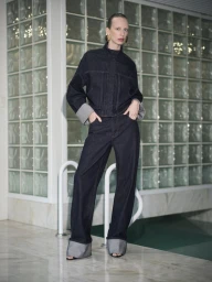 Model Lili Sumner wearing dark denim jacket and pants standing poolside for Sass & Bide Winter 2025 campaign.