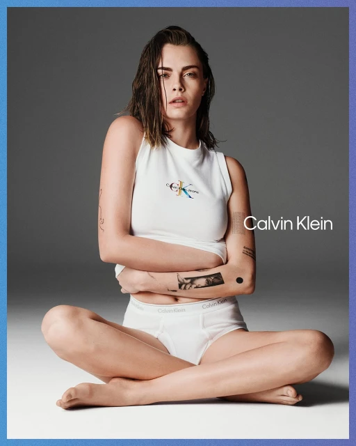 Close-up shot of model Cara Delevingne in a Calvin Klein ad, posing cross-legged on the floor in a white tank top and briefs.