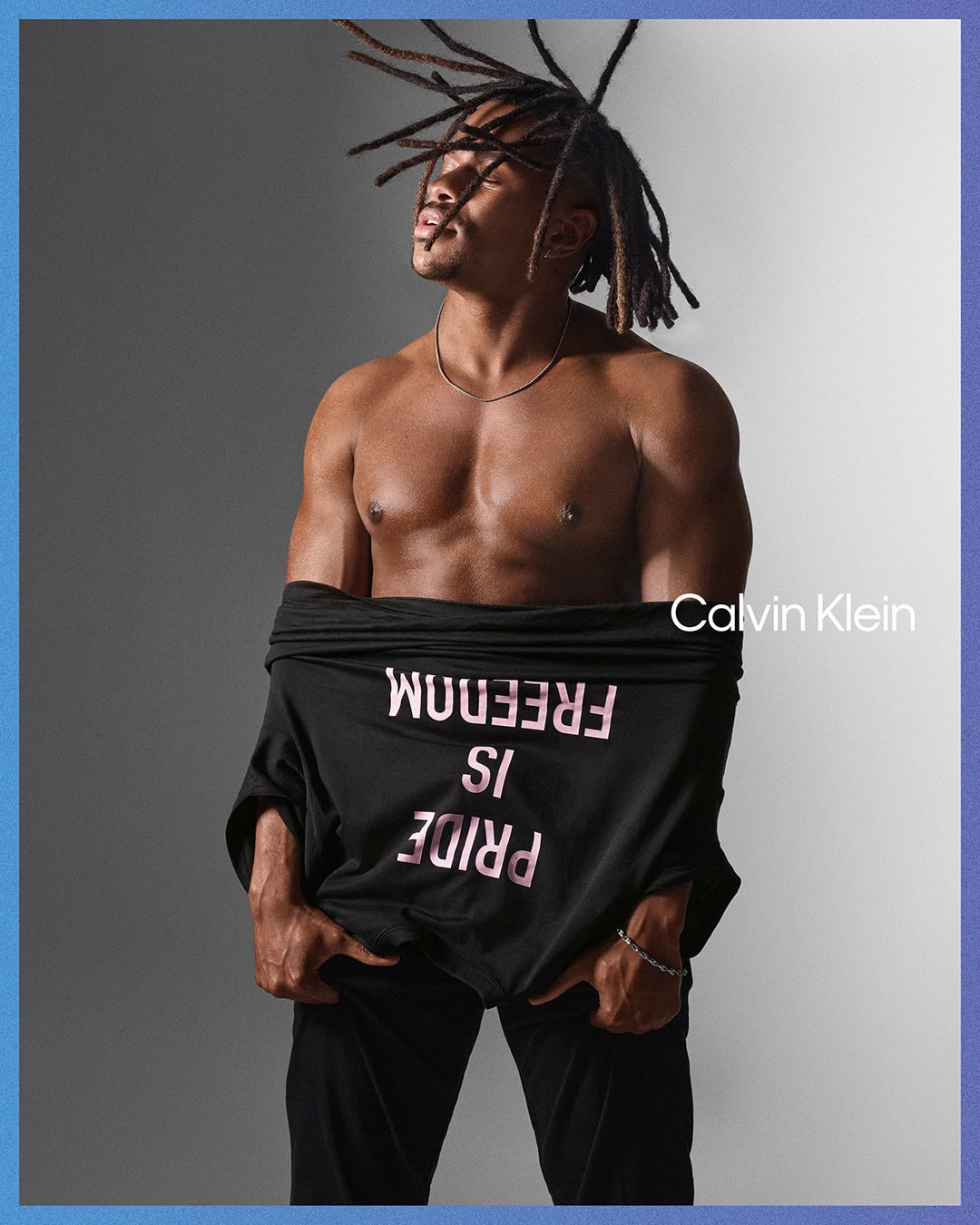 Jeremy Pope with locs wearing a black Calvin Klein t-shirt with inverted text against a split grey and white studio background